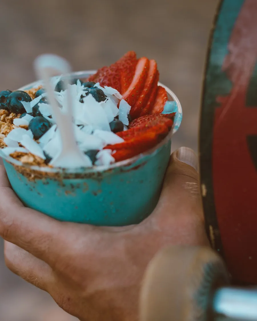 Açaí servido no copo com morangos e mirtilos, segurado na mão